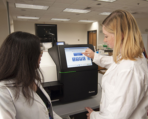 Dr. Baker and team member Anne Atkins, MPH, with the new DNA sequencing instrument, which can detect the gene mutations responsible for 97 percent of CF cases.